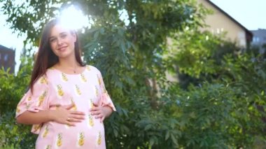 Karnı günbatımında okşayarak pembe elbiseli güzel hamile kız.