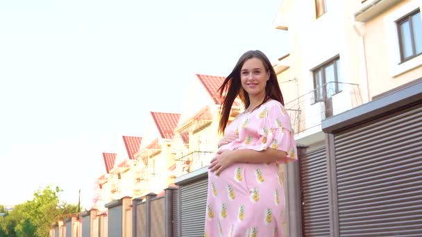 Hermosa chica embarazada en un vestido rosa acariciando su barriga al atardecer . — Vídeos de Stock