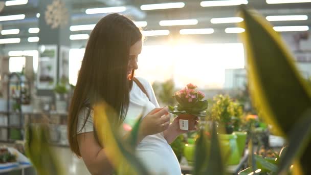 Vacker flicka i en vit T-shirt att köpa grön blomma växter på blomsteraffär. — Stockvideo