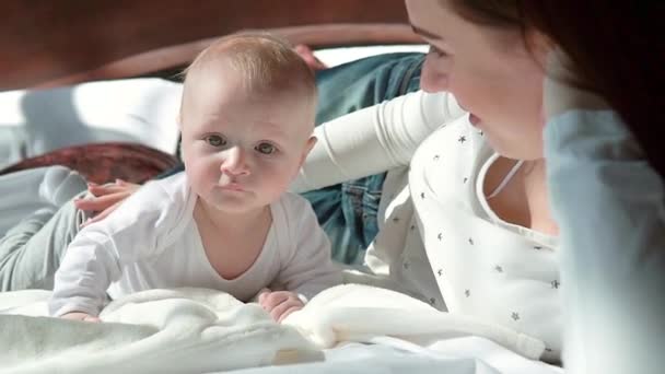 Retrato de cerca de una hermosa madre sonriendo con el bebé en la cama . — Vídeo de stock