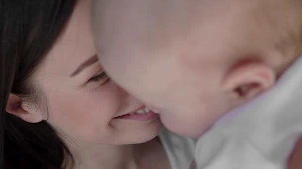 Retrato de cerca de una hermosa madre sonriendo con el bebé en la cama . — Vídeos de Stock