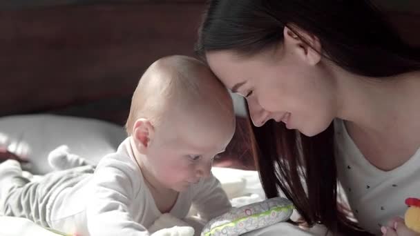 Retrato de cerca de una hermosa madre sonriendo con el bebé en la cama . — Vídeos de Stock