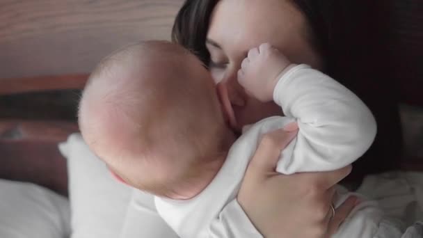 Retrato de cerca de una hermosa madre sonriendo con el bebé en la cama . — Vídeo de stock