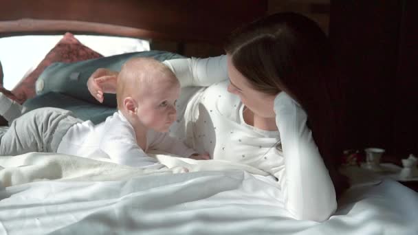 Close-up portret van een mooie moeder lacht met baby in bed. — Stockvideo