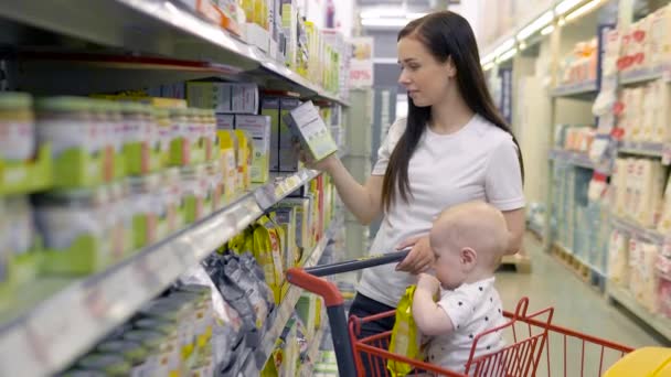 Женщина с маленьким сыном делает покупки в супермаркете, молодая мать задыхается от еды для ребенка на рынке — стоковое видео