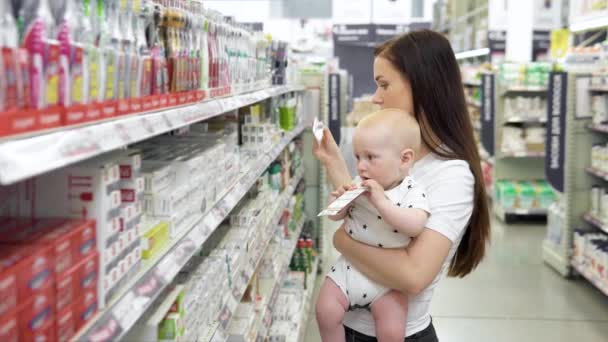 Hermosa mujer con bebé hijo de compras en el supermercado, la joven madre elige cepillos de dientes para su familia en el mercado — Vídeos de Stock