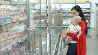Süpermarkette alışveriş bebek oğlu ile güzel kadın, genç Anne pazarda çocukları için yiyecek seçer
