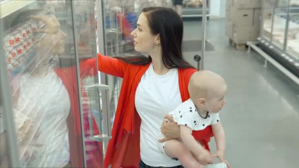 Gyönyörű nő, Baby Son Shopping a szupermarketben, fiatal anya kiválasztja az élelmiszert a gyermek a piacon — Stock videók