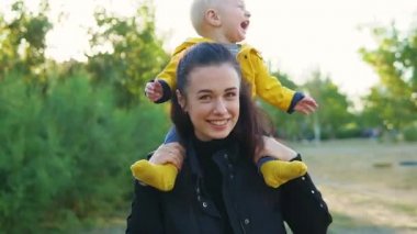 Annem gün batımında parkta çocuğuyla oynuyor. Çocuk sarı bir ceket omuzlarında oturur ve mutlu bir şekilde gülümsüyor. Birlikte dön.