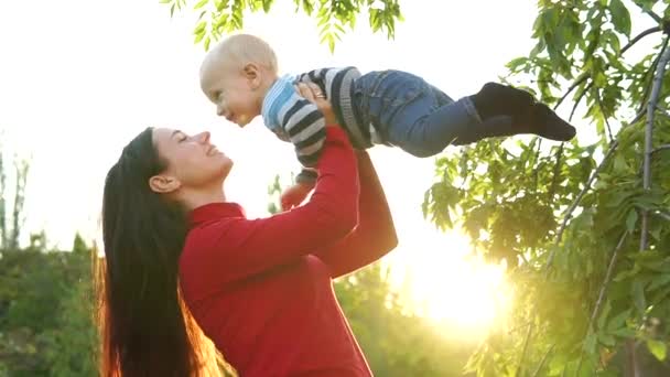 Uma jovem mãe e seu filhinho riem, rodopiam e brincam contra o pano de fundo dos raios brilhantes do sol poente. Cores saturadas bonitas . — Vídeo de Stock