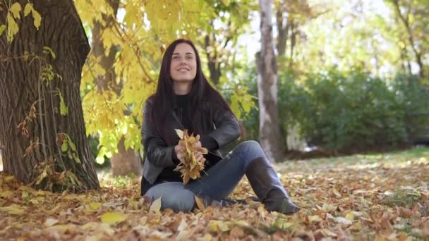 Portret van een schattig meisje dat in het najaarspark gele bladeren opgeeft en prachtig glimlacht. — Stockvideo