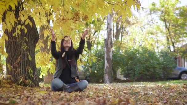 Portret van een schattig meisje dat in het najaarspark gele bladeren opgeeft en prachtig glimlacht. — Stockvideo