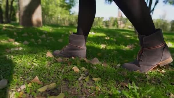 Mladá dívka kráčí po svěží, zelené, podzimní trávě, v hnědých botách, v parku. Dívčí nohy kloužou ve zpomaleném pohybu po spadlých podzimních listech. — Stock video