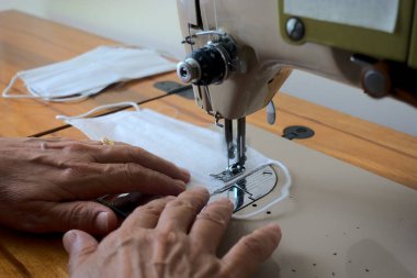 Yakın çekim yüzüklü kadın dikiş makinesi kullanarak cerrahi maske üretiyor.