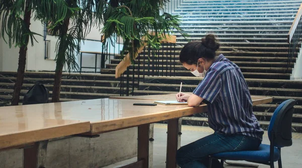 孤独的长发蒙面的年轻大学生独自在图书馆学习 图库图片