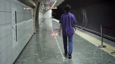 Maskeli, uzun saçlı yetişkin yürüyüşleri, kulaklığından müzik dinlemek ve metronun gelmesini beklerken edebiyat kitabı okumak.