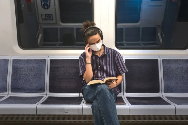 Soyutlanmış ve maskeli zeki genç bir adam müzik dinliyor ve metroda seyahat ederken edebiyat kitabı okuyor.