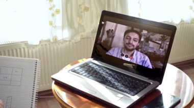 Evde çalışan orta yaşlı, gülümseyen bir adam bilgisayarını kullanarak aldığı bir video görüşmesini not alıyor.