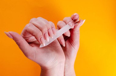 Turuncu bir arka plan üzerinde cam törpü ile manikür yapıyor kadın