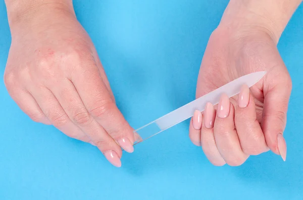 Mavi bir arka plan üzerinde cam törpü ile manikür yapıyor kadın