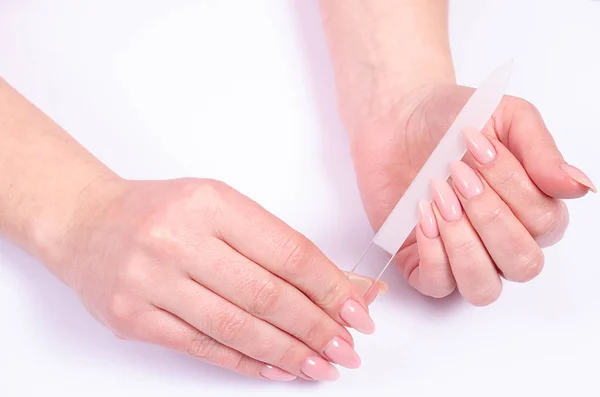 Woman doing a manicure with a nail file on a gray background
