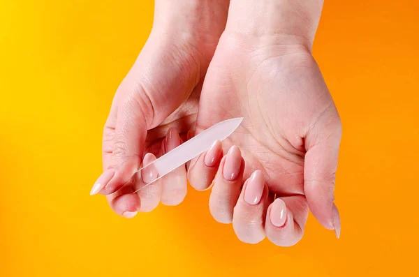 Turuncu bir arka plan üzerinde cam törpü ile manikür yapıyor kadın