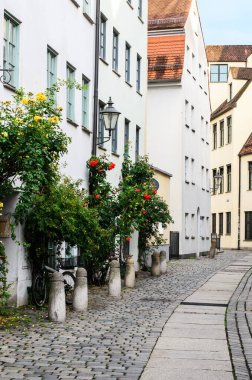 AUGSBURG, GERMANY 27 HAZİRAN 2025: Kentsel cadde güneşli bir yaz gününde çok az yayaya sahip çok sayıda konut binası ve boş bir açık kafeterya ile sıralanmış 