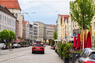 AUGSBURG, GERMANY 27 HAZİRAN 2025: Kentsel cadde güneşli bir yaz gününde çok az yayaya sahip çok sayıda konut binası ve boş bir açık kafeterya ile sıralanmış 
