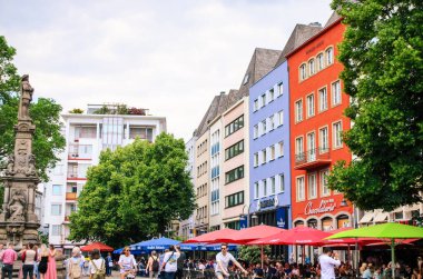 KLN, ALMANY HAZİRAN 2024: İnsanlar yaz günü şehir merkezinde renkli geleneksel evlerle cadde boyunca yürüyorlar