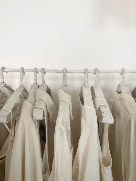 El yapımı bir askıda beyaz bir duvara asılmış bir sürü beyaz keten elbise..
