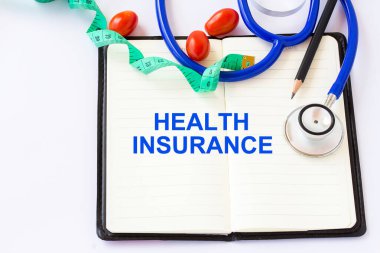 Sağlık sigortası metni, blackground defter stetoskop ve ölçüm tap ile beyaz bir arka plan üzerinde. Sağlık sigortası kavramı