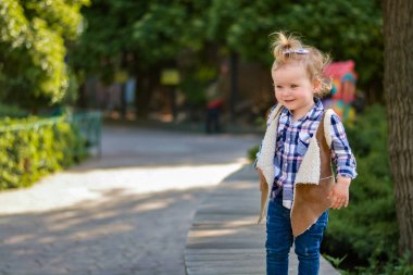 Modaya uygun bir yelek ve dışarıda poz veren kot pantolonlu şirin bir manken. Çocuk giyim koleksiyonları, moda broşürleri, şık giyim promosyonları ve yaratıcı reklamlar için mükemmel stok fotoğrafı..