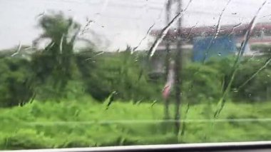 Yağmurlu bir günde Hindistan caddesinde otobüste oturmak. Islak otobüs penceresi 4K. Hint muson yağmurları.