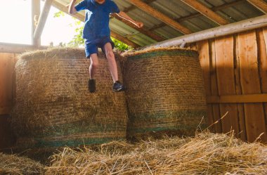 Bir çocuk saman balyasından atlıyor, yüzü görünmüyor, kişiliksizleştirme fotoğrafı.