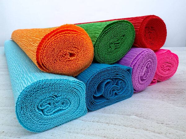 Set of vibrant crepe paper rolls in different colors stacked together on light surface. Perfect material for crafts, DIY projects, handmade decorations, and floral art.