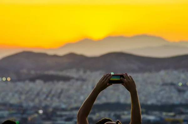 Atina 'nın batısındaki dağlarda gün batımının fotoğrafını çeken bir turist, akıllı telefonuyla Yunanistan' ın batısında