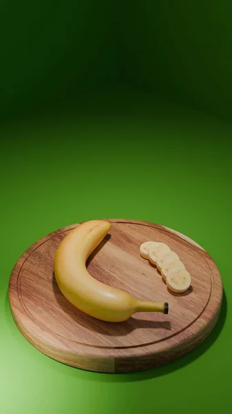 Dilimlenmiş 3 boyutlu muz, tahta bir kesme tahtasının üzerinde, temiz yeşil bir zemine karşı. Kompozisyonda sağlıklı yiyecekler, tropikal meyveler ve modern besinler vurgulanıyor.