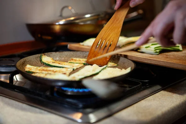 Kızartma tavasında kabak dilimleri pişirip ahşap bir spatulayla çevirin. Evde taze sebzeler pişiriliyor..
