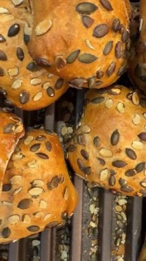 Fırın tepsisine yerleştirilmiş kabak tohumlarıyla dekore edilmiş ekmek rulolarının videosunu kapat. Taze pişmiş çörekler mutfak tasarımı için fotokopi alanı ile sağlıklı bir yiyecek arka planı sağlar.