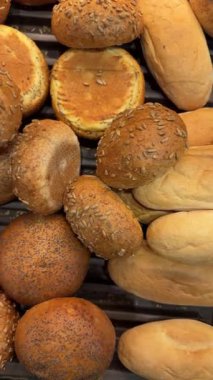 Tepside üst üste dizilmiş çeşitli fırın çörekleri ve küçük ekmek rulolarının videosunu kapat. Altın fırında pişirilmiş ürünler, kopyalama alanı olan desenli gıda arka planı oluşturur.