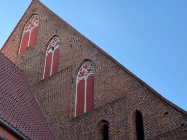 1370 yılında Avrupa 'da inşa edilen ortaçağ gotik tuğla kilisesinin yan görünüşü, sivri kemerli pencereler ve mavi gökyüzüne karşı kırmızı boyanmış detaylar.