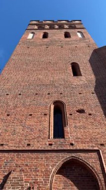 Orta çağ gotik tuğla kilise kulesinin dar kemerli pencereli dikey videosu. Perspektifte kale benzeri mimari ve kültür mirası vurgulanıyor.