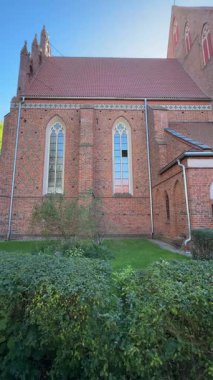 Geçmişi 14. yüzyıla dayanan tarihi Gotik Katolik kilisesi uzun tuğlalı duvarlar, kemerli pencereler ve çevreleyen yeşillikler.