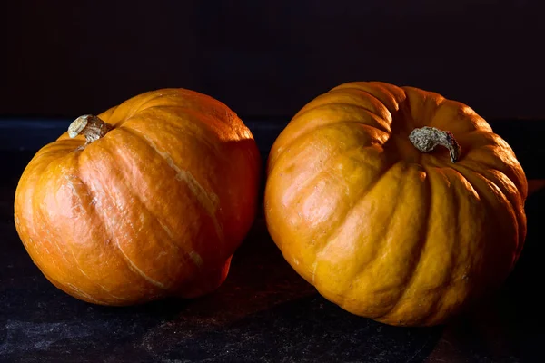 Pair of pumpkins photographed on black studio background. Minimalist autumn Halloween theme composition.
