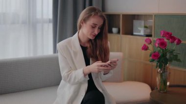 Akıllı telefonuyla mesajlaşırken gülümseyen kadın, elinde telefonla fintech, bankacılık ve modern bir odadaki koltukta cep telefonu, kredi kartı ve akıllı telefon ile basit bir işlemle gülümseyen kadın.