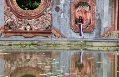 Hoi An, Vietnam 'da, Ağustos 2019' da Tam Quan kapısının çeşmesine yansıyan kız, ya da üç girişli kapı, 1626 'da inşa edilen ve Ba Mu Tapınağı olarak bilinen eski tapınak kompleksine açılıyor.