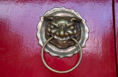 Bronze door knocker on the red door of Fukian Assembly Hall or Phuc Kien in the Hoi An ancient town in Quang Nam Province of Vietnam clipart
