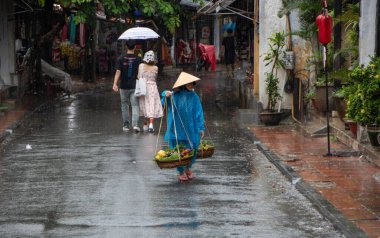 Hoi An - Vietnam - Ağustos 2019 - Kadınlar omuzlarında geleneksel ağırlıkla meyve satıyorlar - eski şehrin caddesi