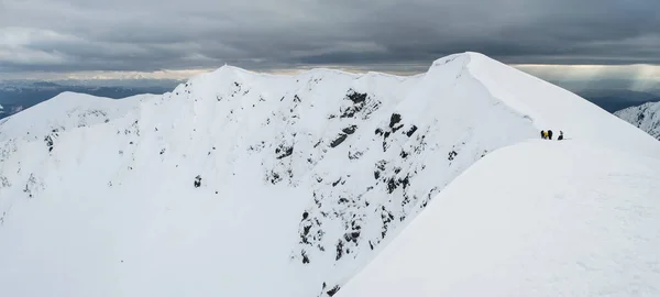 Panoramic view of snowy mountain range with hikers on it in cloudy winter day