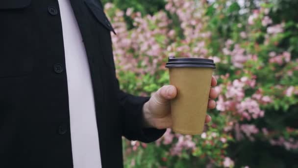 Man houdt koffie op de achtergrond van mooie bloemen in het park — Stockvideo